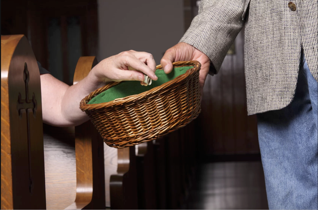mãos depositando envelope de dízimo em cesto de ofertas durante missa católica