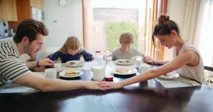 família rezando antes das refeições com uma criança em casa