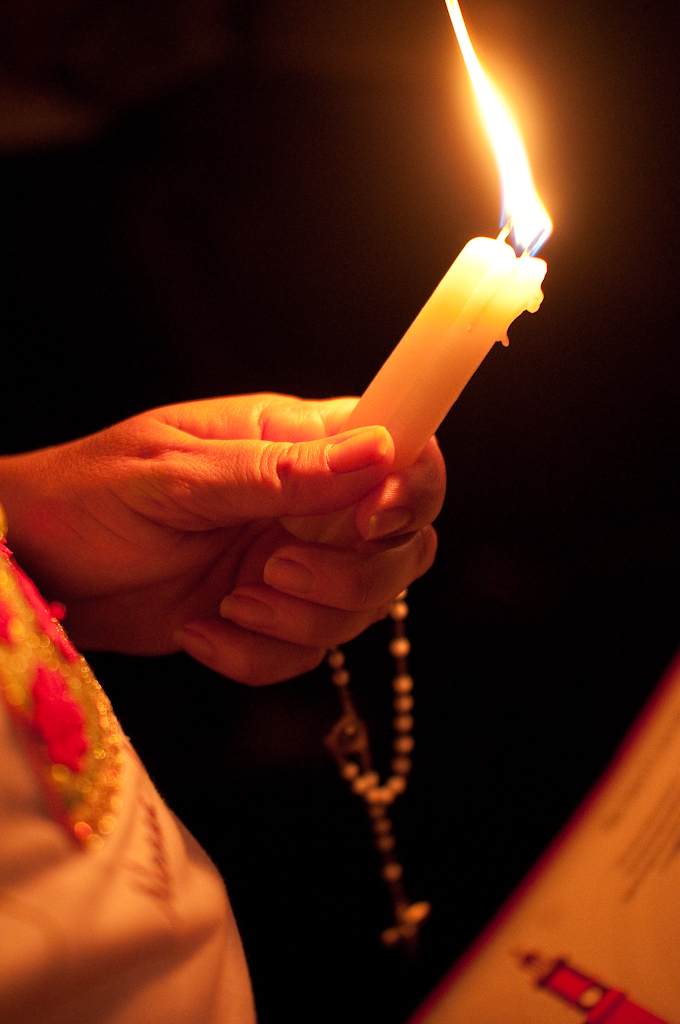 Como rezar pelas almas do Purgatório e o valor das Missas de Sétimo Dia 8 Mãos rezando um terço diante de uma vela, ambiente de igreja